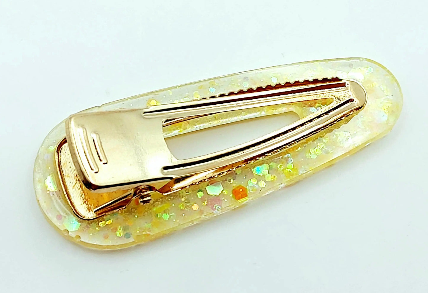 Barrette à cheveux arrondie en résine époxy. Jaune translucide et paillettes holographiques. Vue de l'envers.
