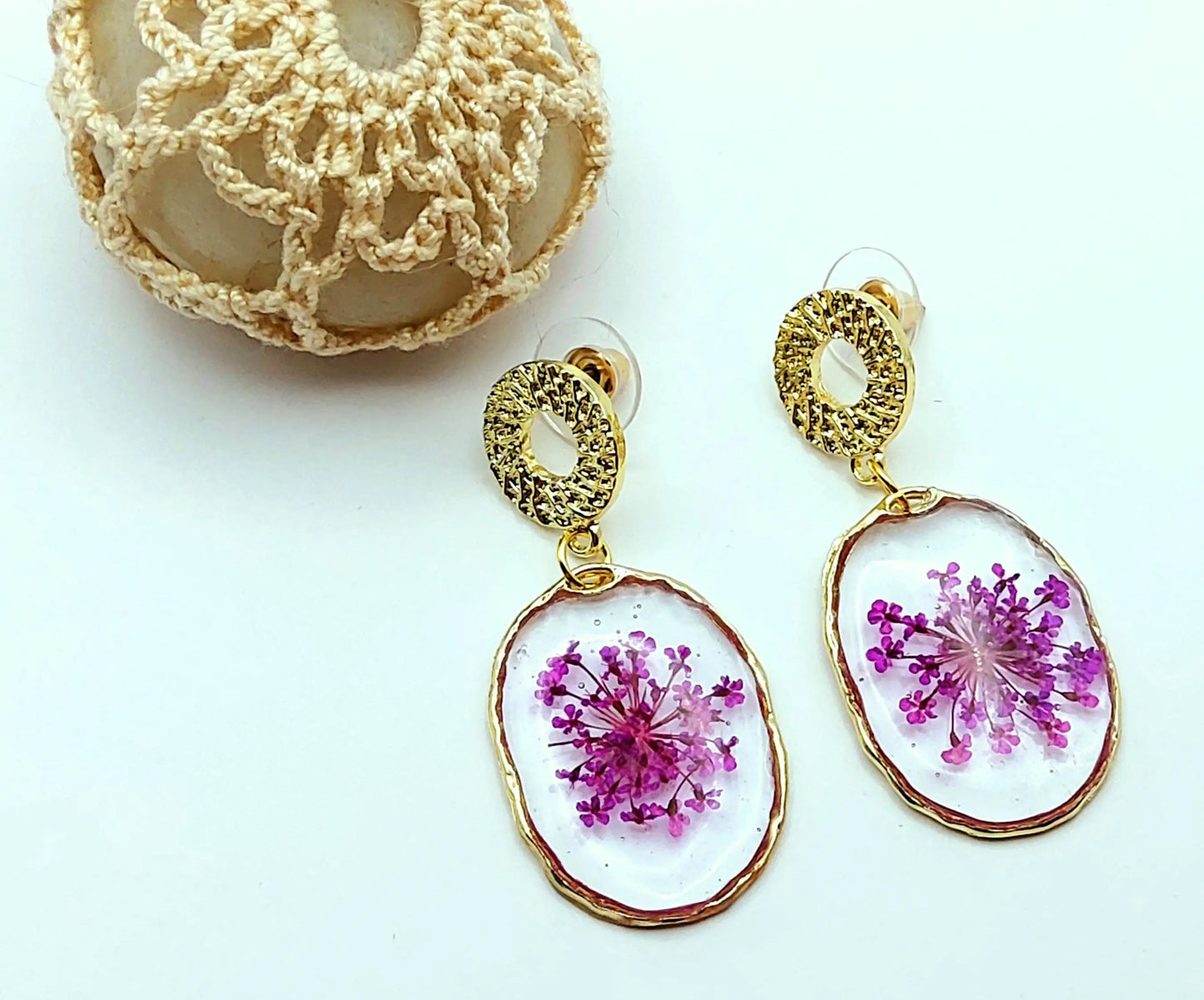 Boucles d'oreilles en résine "Fleurs violettes", posées devant un galet