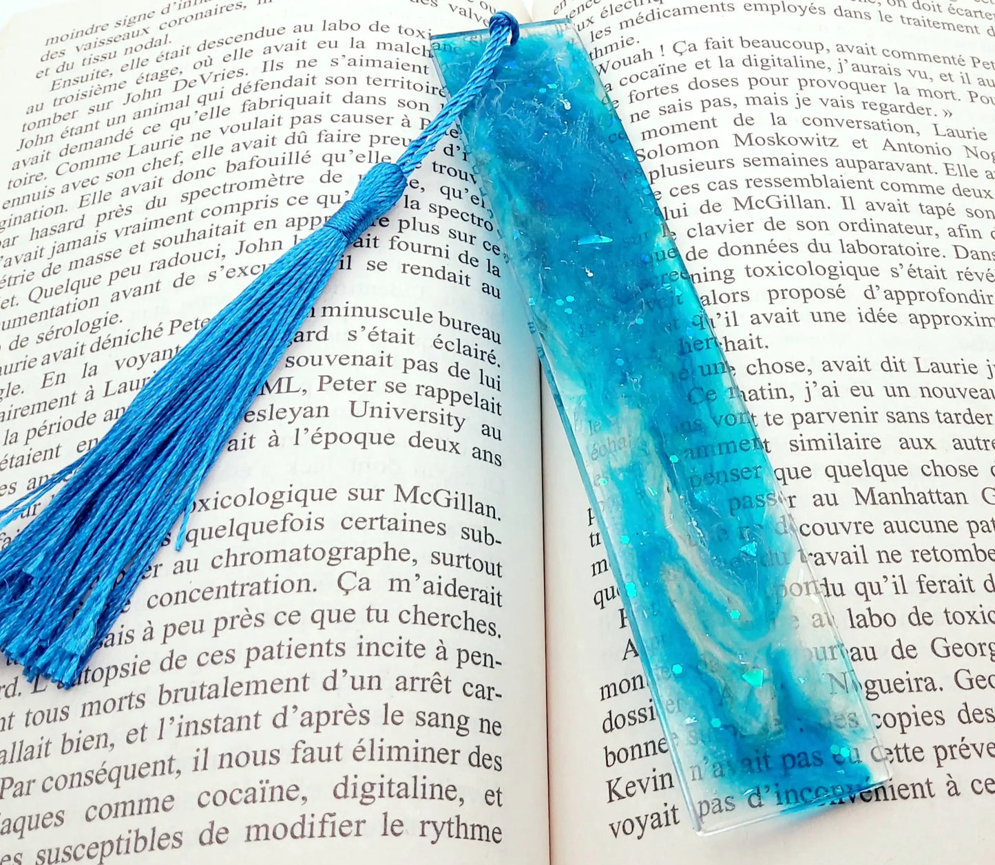 Marque-pages en résine époxy, marbré bleu, pompon gland soyeux bleu, posé dans un livre