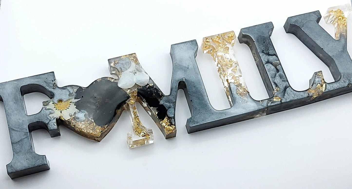 Mot décoratif "FAMILY" en résine époxy. Gris argenté, fleurs noires et blanches. Feuille d'or.