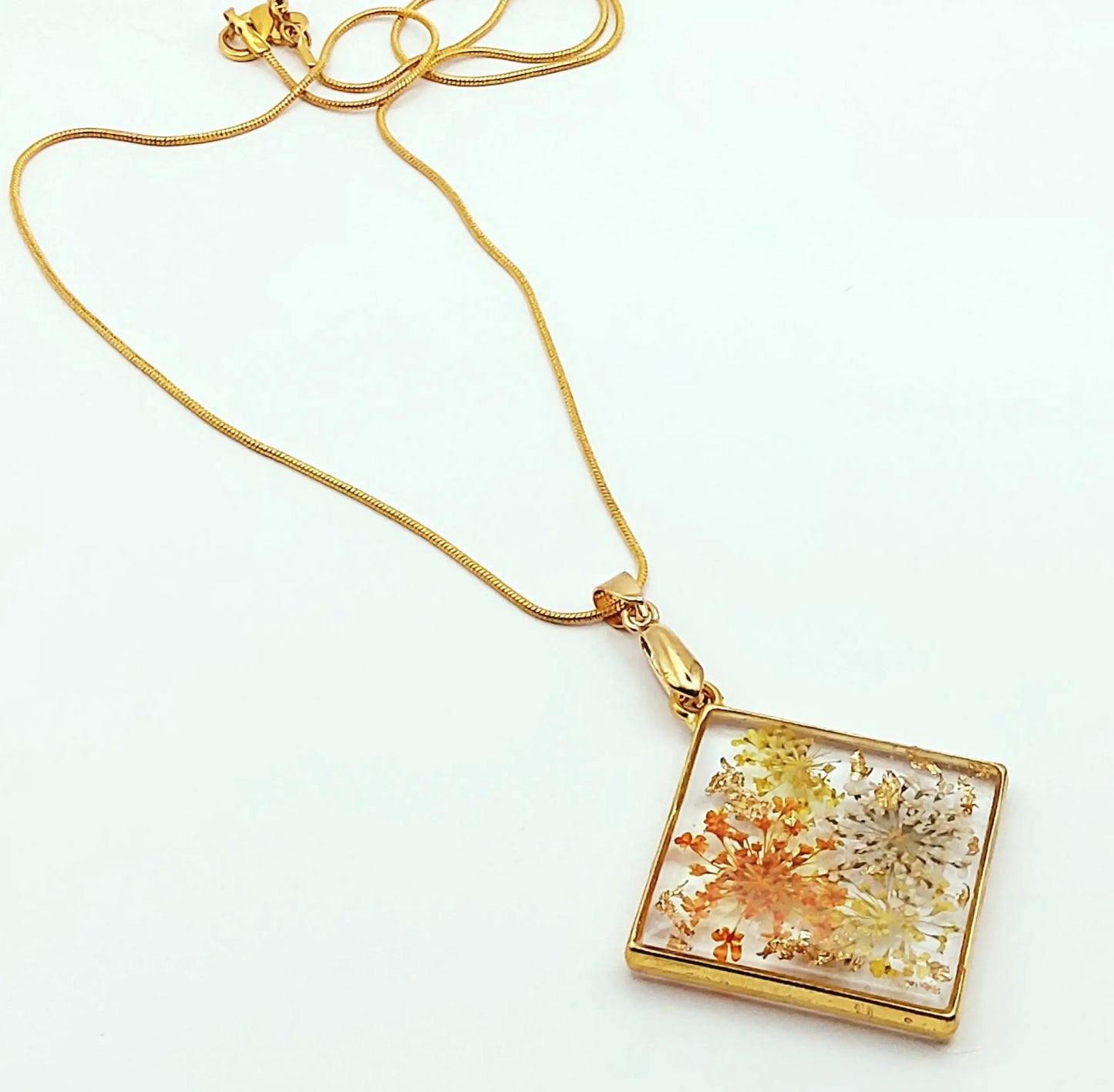 Pendentif Carré en résine et sa chaîne dorée, fleurs oranges et jaunes. Plan large.