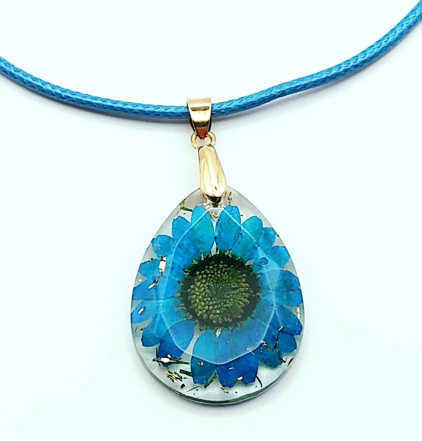 Pendentif OVALE en résine époxy. Fleur bleue et paillettes dorées. Cordon en coton ciré bleu.