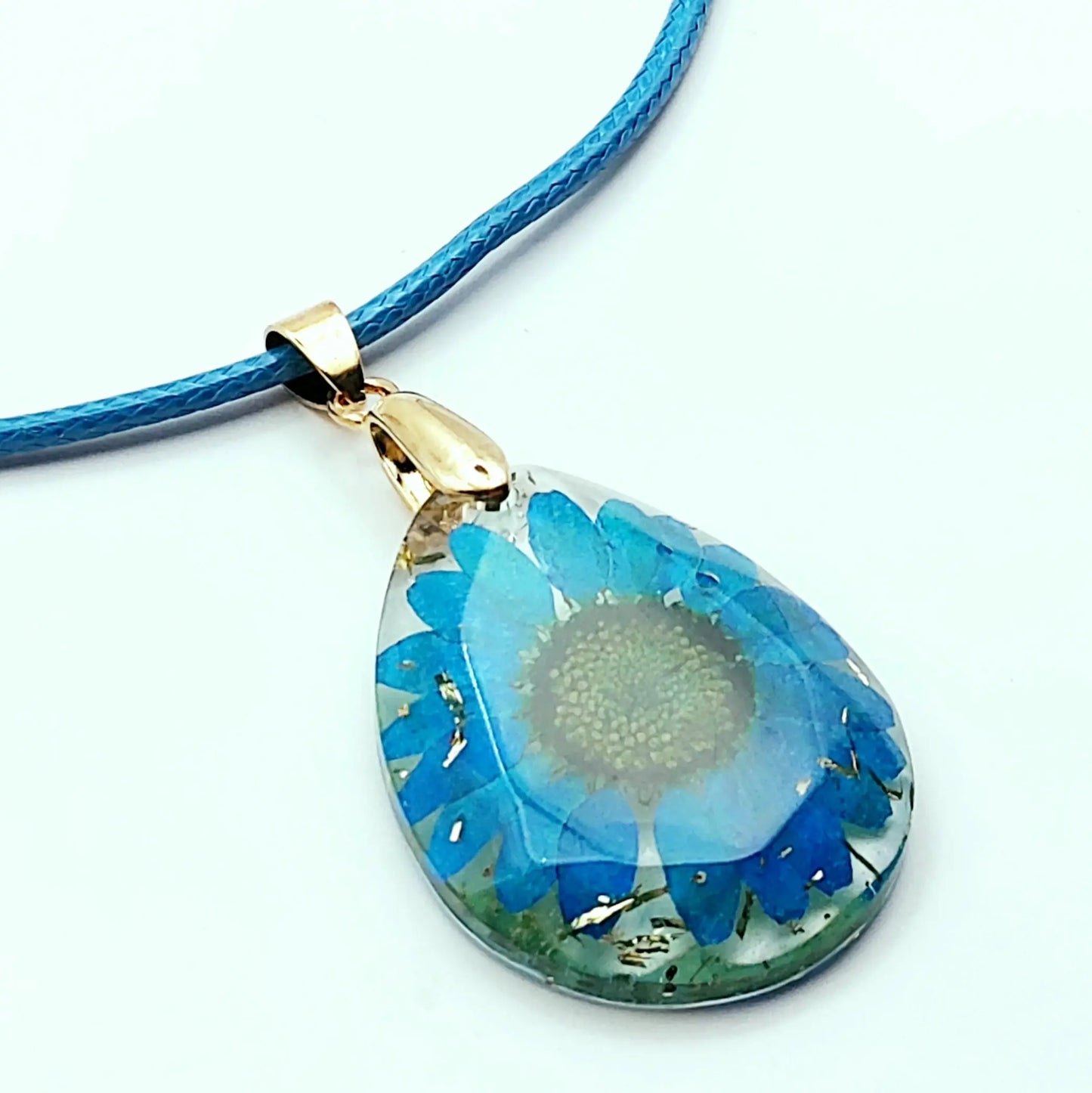 Pendentif OVALE en résine époxy. Fleur bleue et paillettes dorées. Cordon en coton ciré bleu.