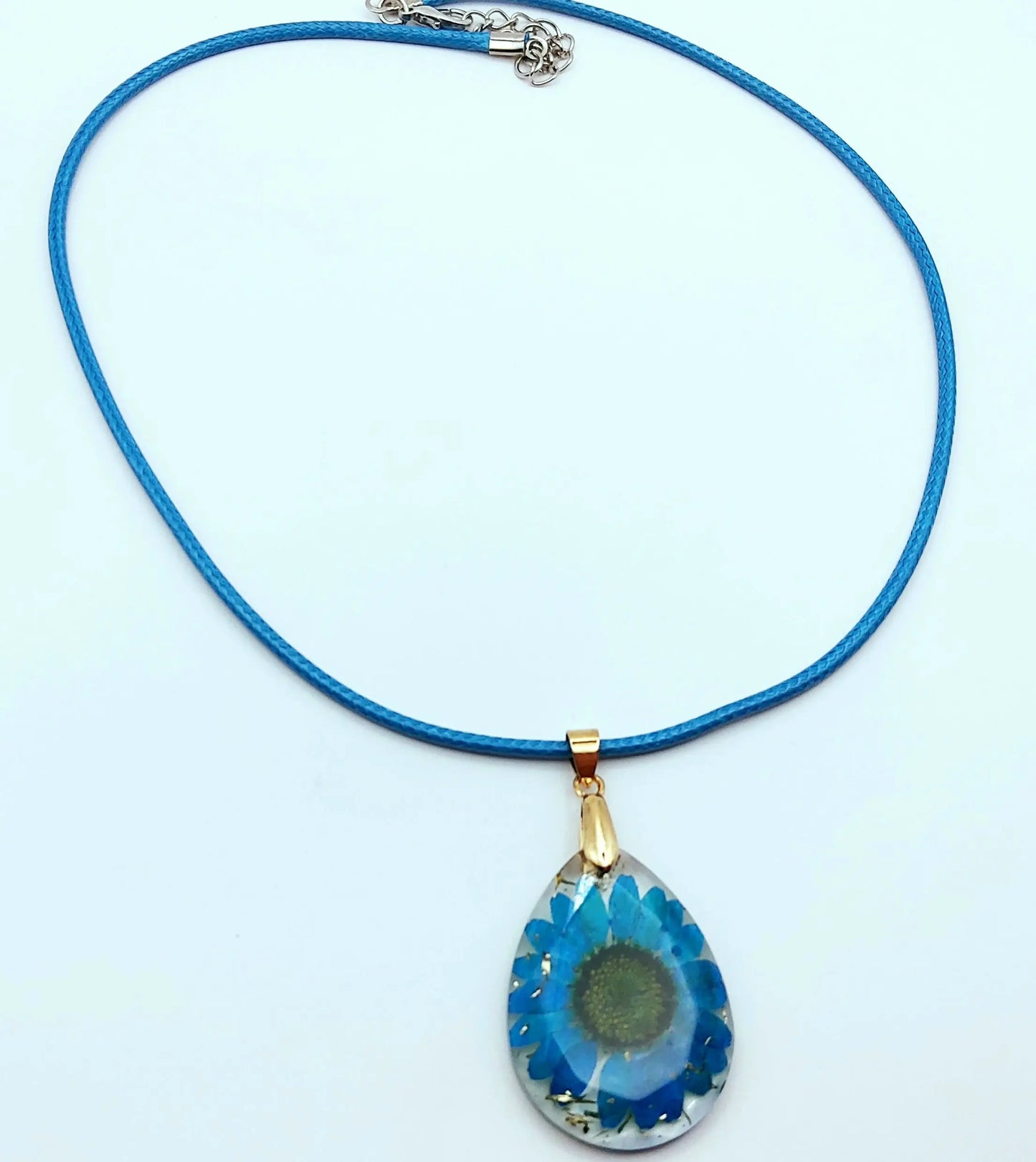Pendentif OVALE en résine époxy. Fleur bleue et paillettes dorées. Cordon en coton ciré bleu.