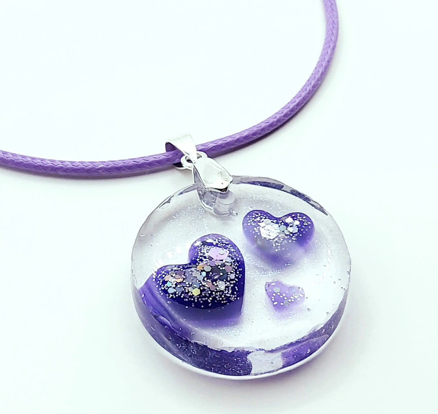 Pendentif ROND en résine époxy. Transparent avec effet irisé. Renferme 3 petits cœurs violets et paillettes argentées. Cordon en coton ciré mauve. PRETTY RESINE