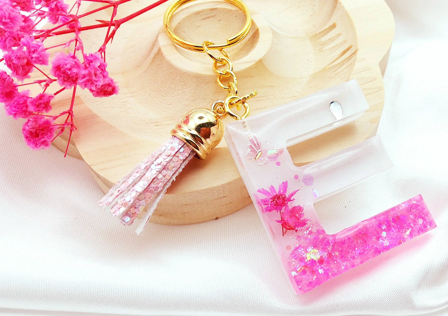 Porte-clés LETTRE E en résine époxy. Fond blanc. Paillettes, fleurs et papillon roses. Pompon gland pailleté rose. PRETTY RESINE