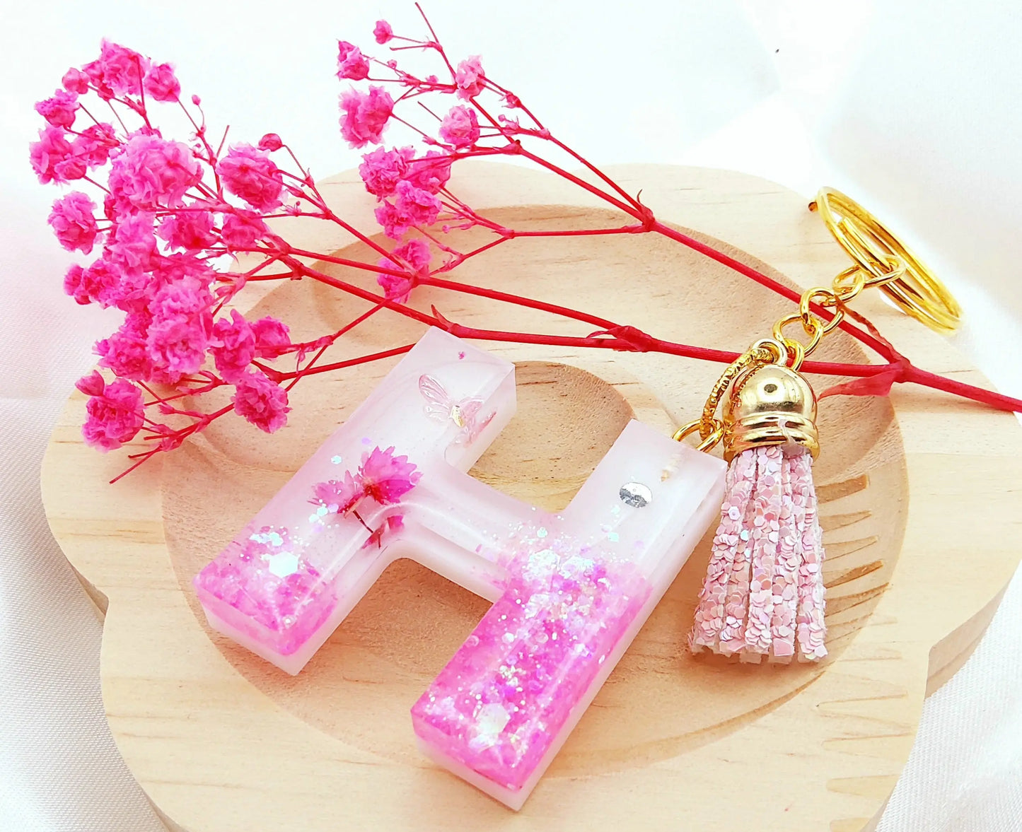 Porte-clés LETTRE H en résine époxy. Fond blanc. Paillettes, fleurs et papillon roses. Pompon gland pailleté rose - PRETTY RESINE
