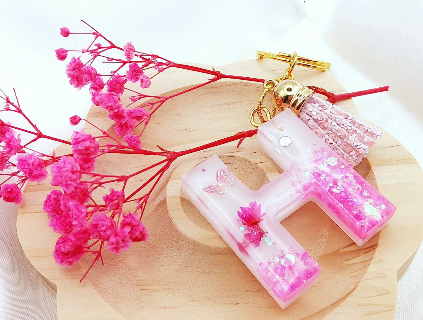 Porte-clés LETTRE H en résine époxy. Fond blanc. Paillettes, fleurs et papillon roses. Pompon gland pailleté rose - PRETTY RESINE