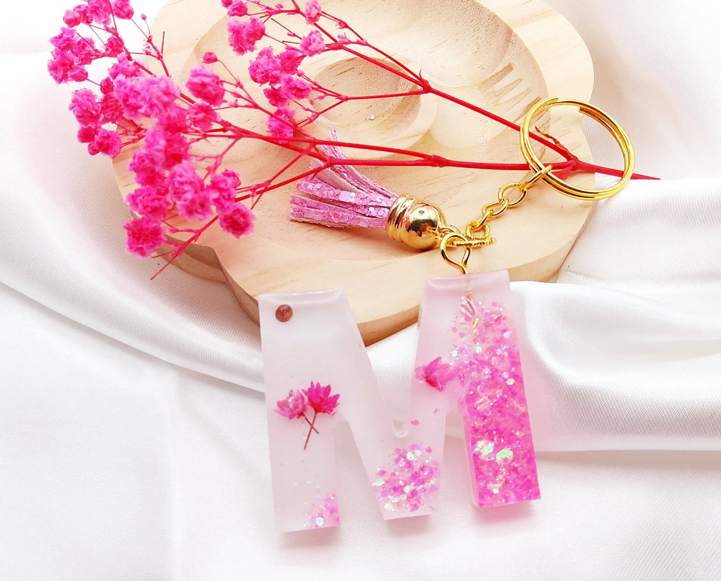 Porte-clés LETTRE M en résine époxy. Fond blanc. Paillettes, fleurs et papillon roses. Pompon gland rose. PRETTY RESINE