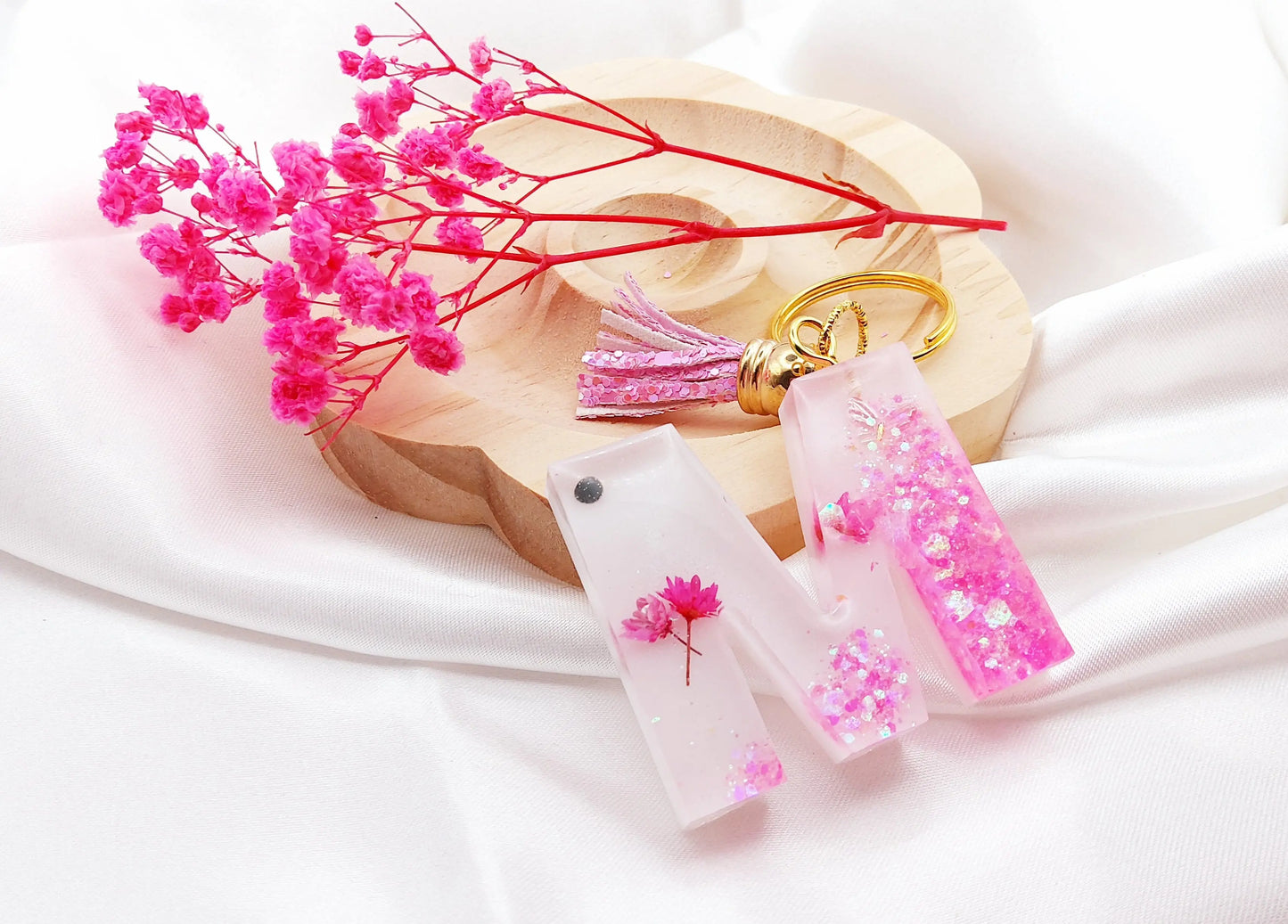 Porte-clés LETTRE M en résine époxy. Fond blanc. Paillettes, fleurs et papillon roses. Pompon gland rose. PRETTY RESINE