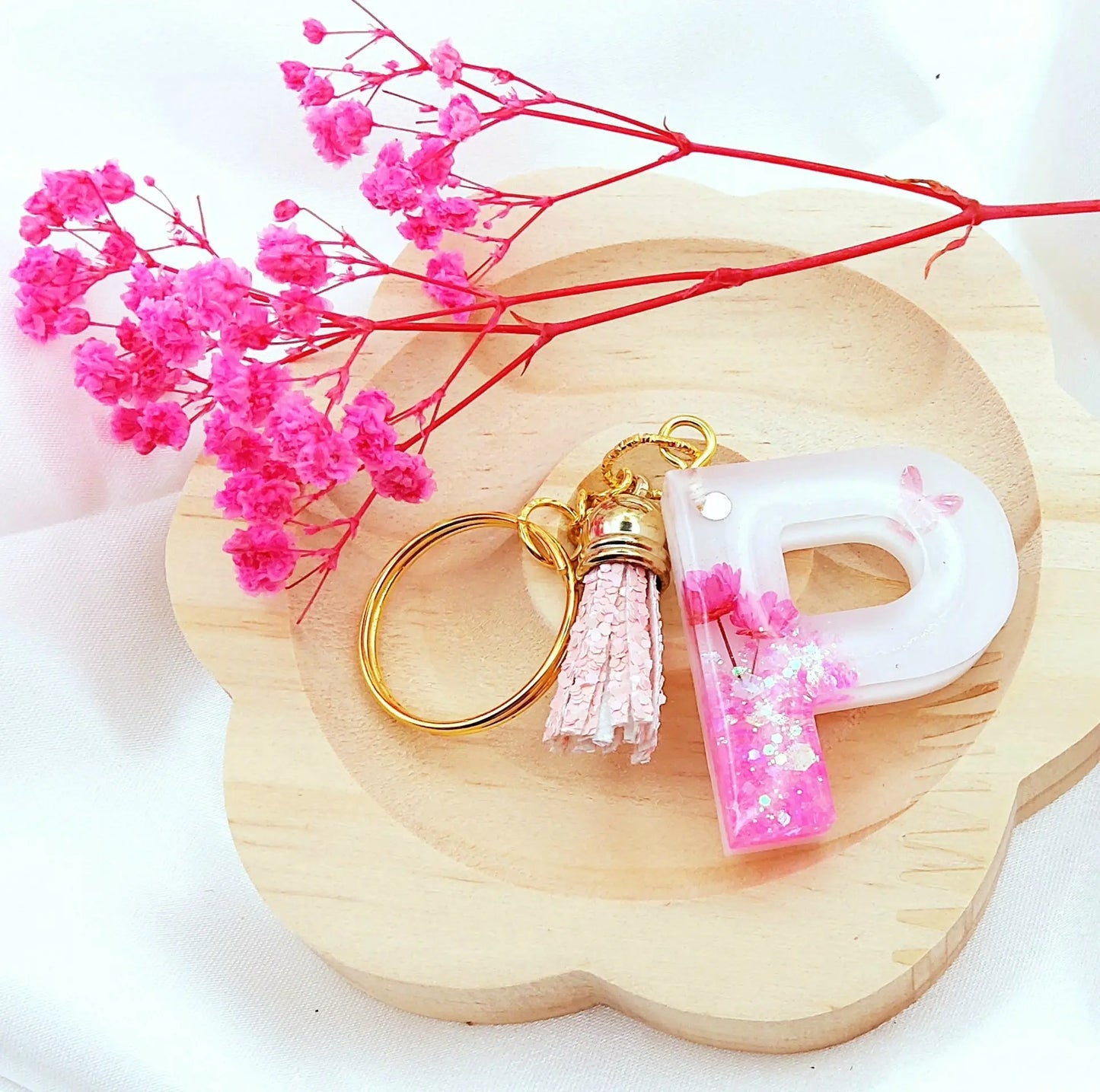 Porte-clés LETTRE P en résine époxy. Fond blanc. Paillettes, fleurs et papillon roses. Pompon gland pailleté rose. PRETTY RESINE