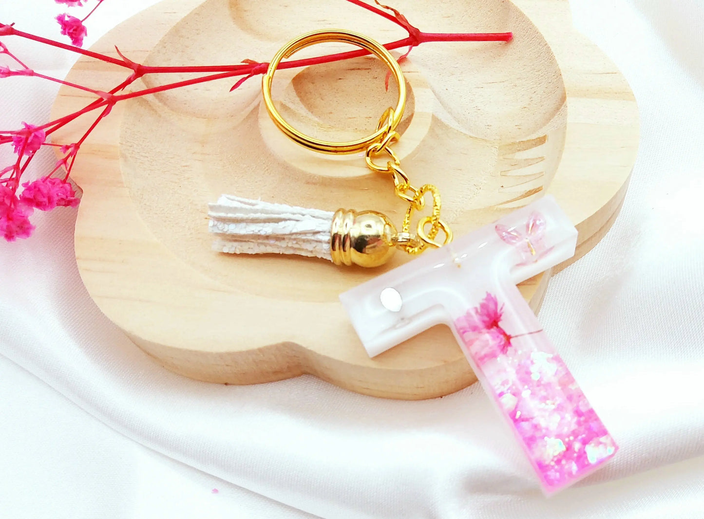 Porte-clés LETTRE T en résine époxy. Fond blanc, paillettes, fleurs et papillon roses. Pompon gland pailleté blanc. PRETTY RESINE