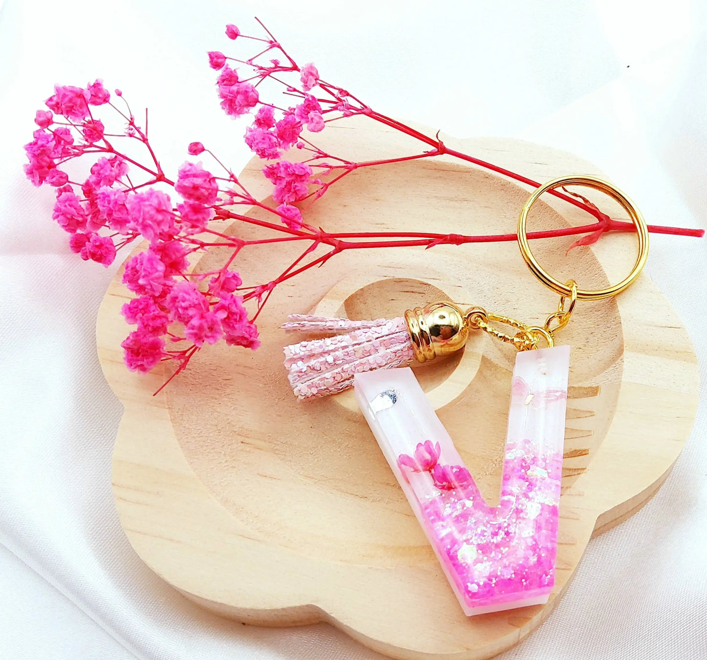 Porte-clés LETTRE V en résine époxy. Fond blanc. Paillettes, fleurs et papillon roses. Pompon gland pailleté rose. PRETTY RESINE