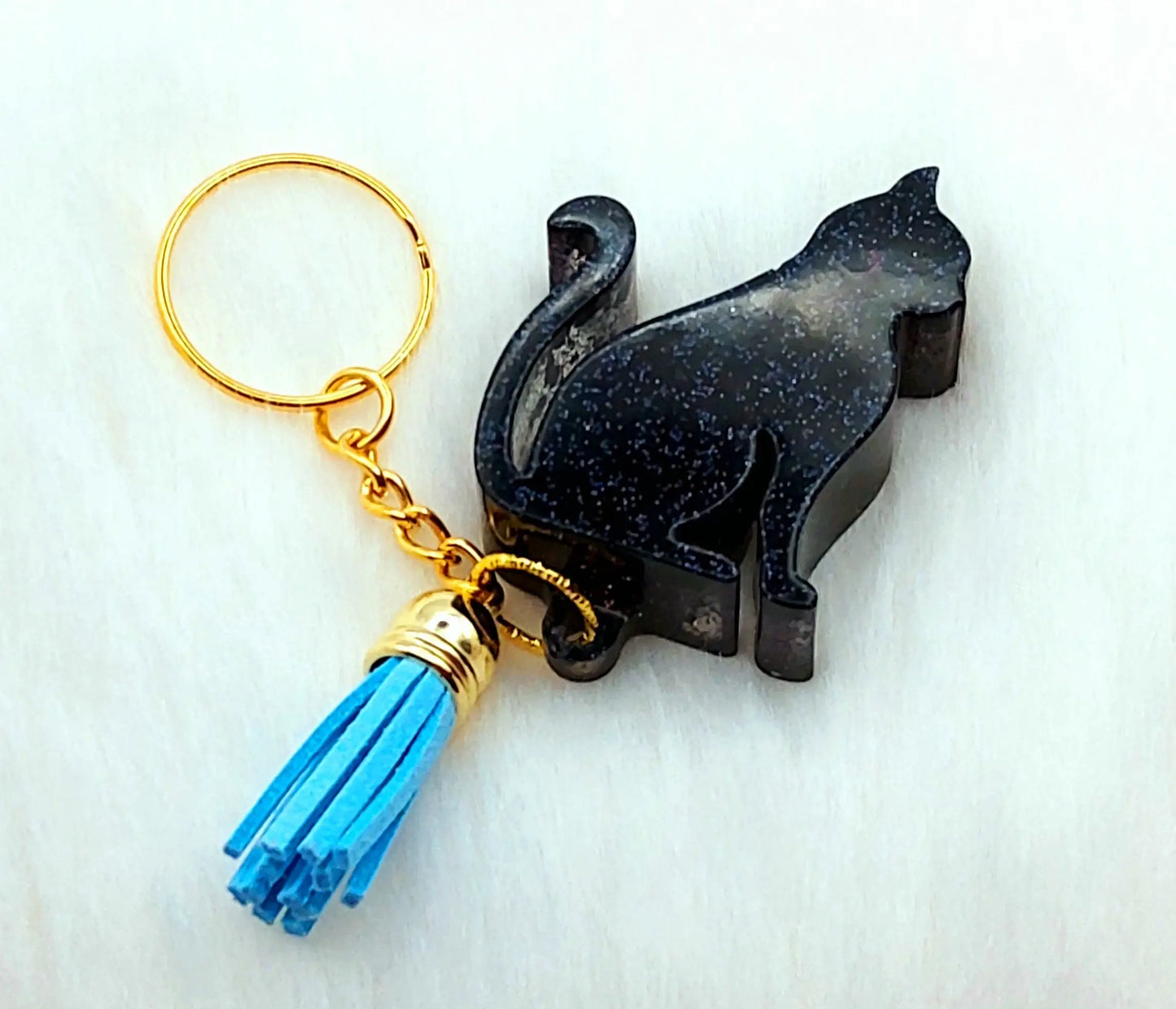 Porte-clés CHAT ASSIS en résine. Noir pailleté et pompon gland bleu.