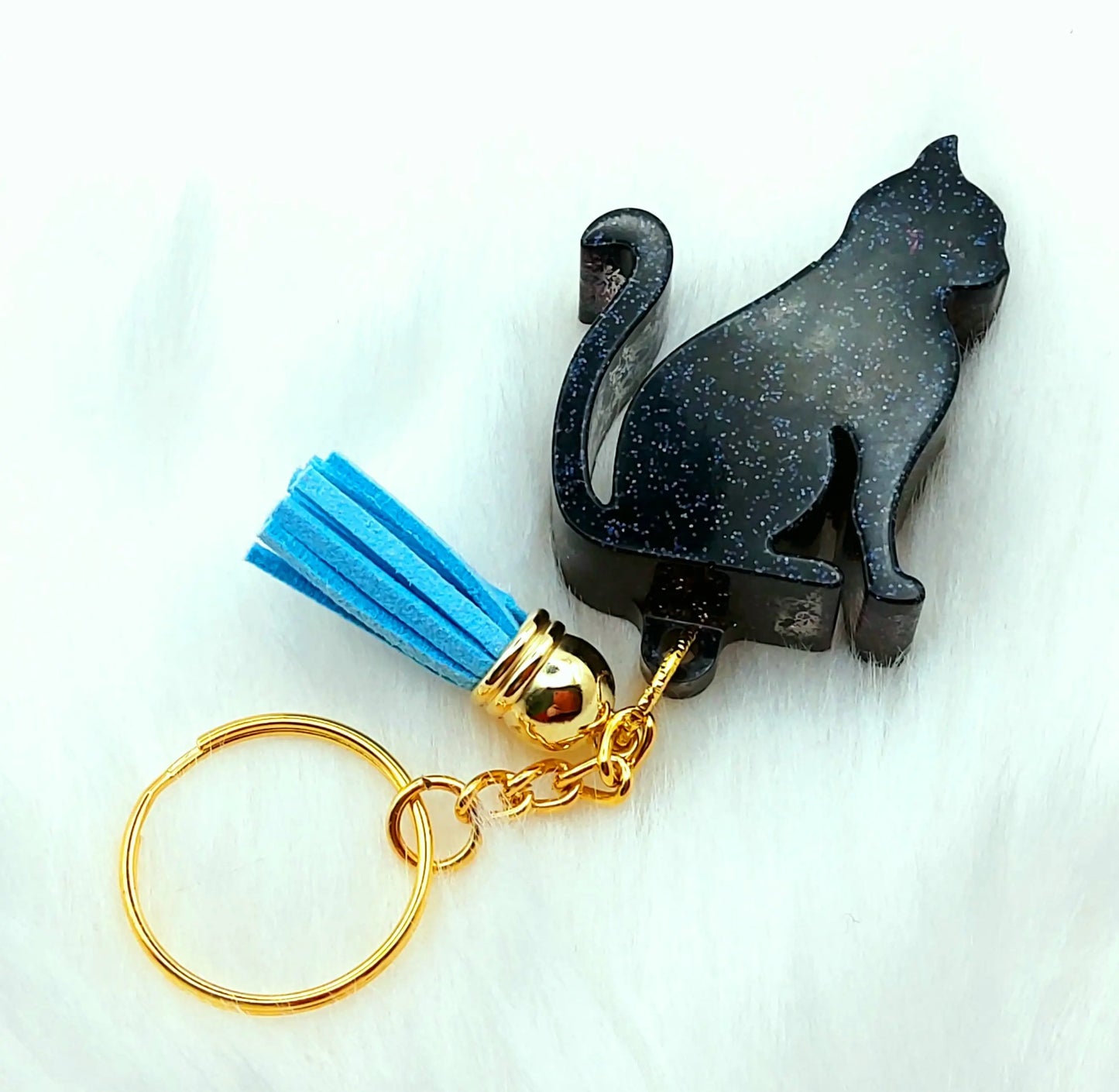 Porte-clés CHAT ASSIS. Noir pailleté, anneau doré, pompon gland bleu.