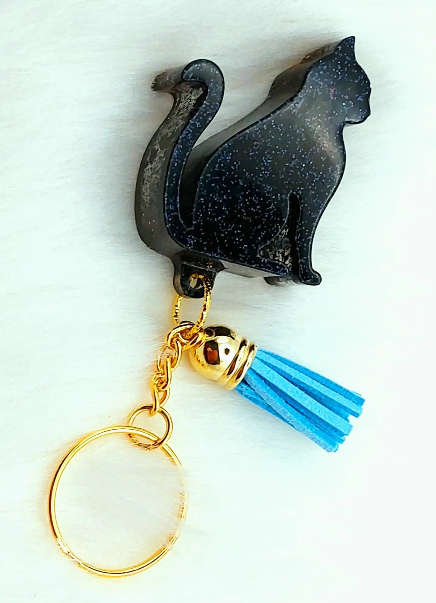 Porte-clés CHAT ASSIS en résine. Noir pailleté et pompon gland bleu.