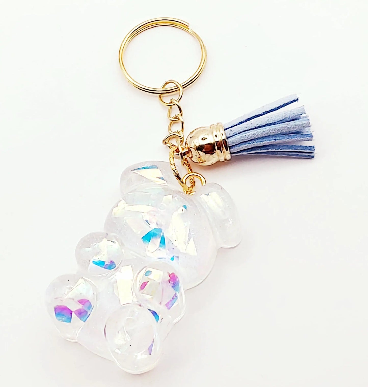 Porte-clés "Ourson debout" en résine époxy. Transparent et holographique. Anneau doré, pompon gland bleu clair.