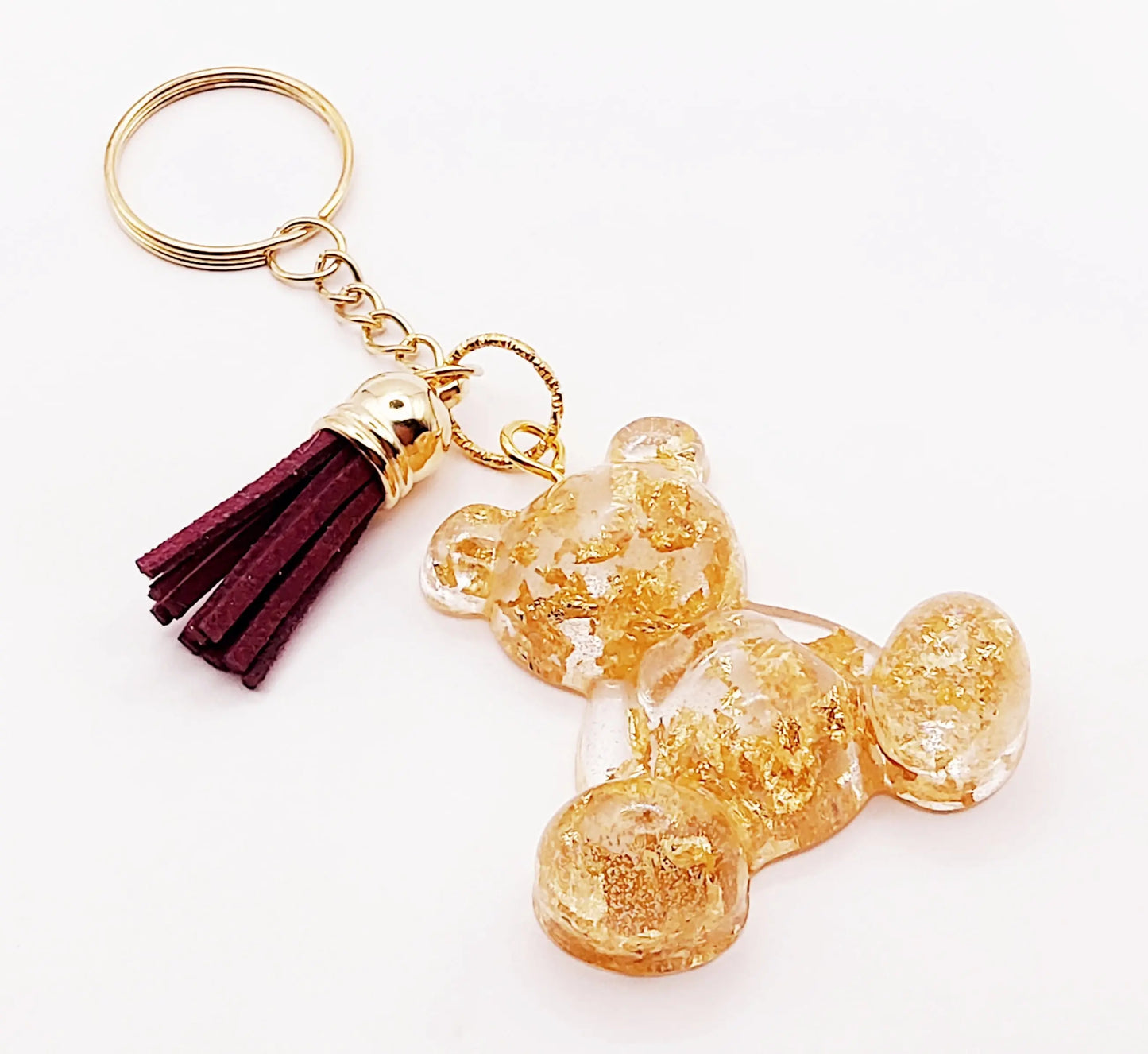 Porte-clés "Ourson assis" en résine époxy. Transparent avec feuille d'or. Anneau doré. Pompon gland prune.