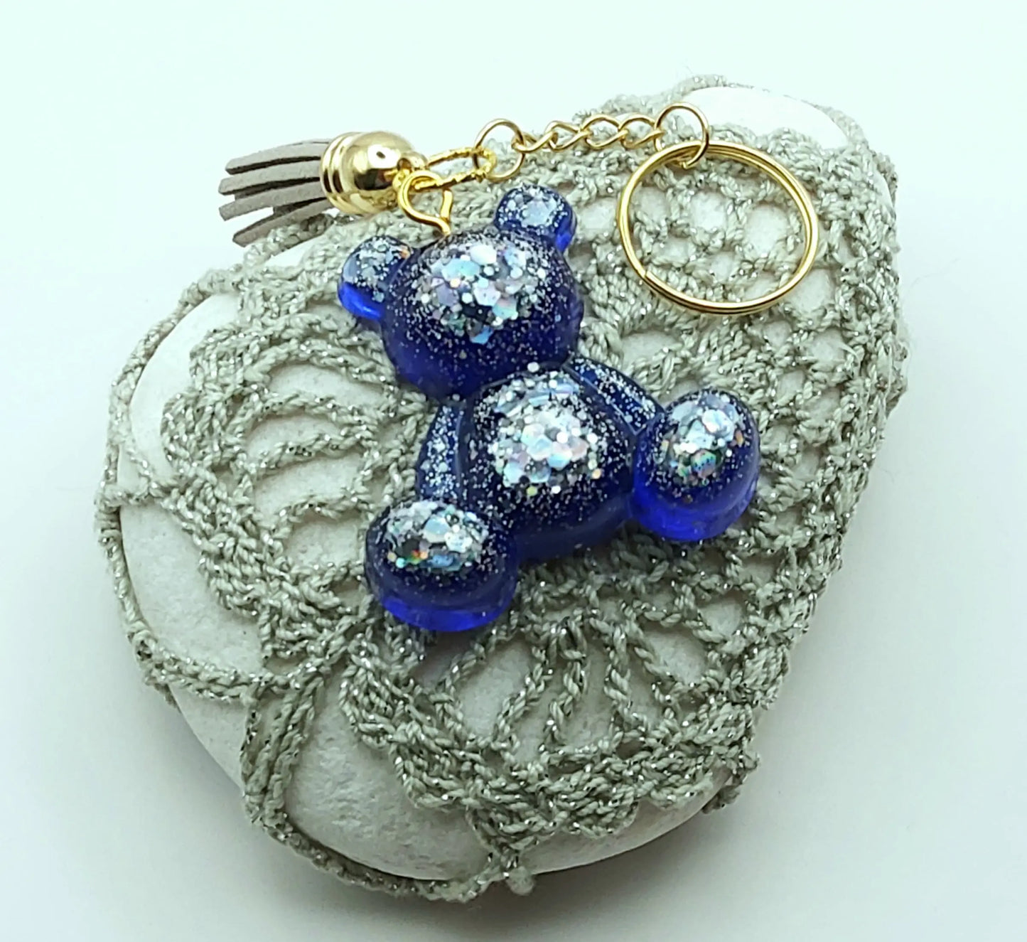 Porte-clés "Ourson assis" en résine époxy, bleu marine et paillettes argentées. Anneau doré. Pompon gland gris clair. Posé sur un galet.