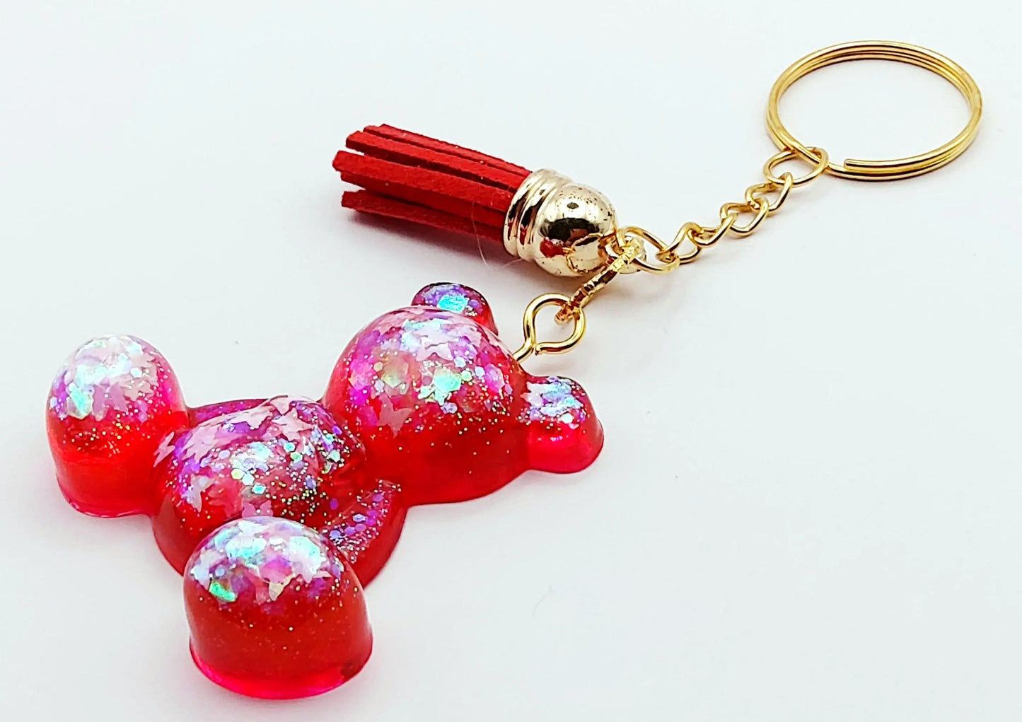 Porte-clés "Ourson assis" en résine époxy. Rouge translucide et paillettes papillons holographiques. Anneau doré. Pompon gland rouge. Vue de côté.