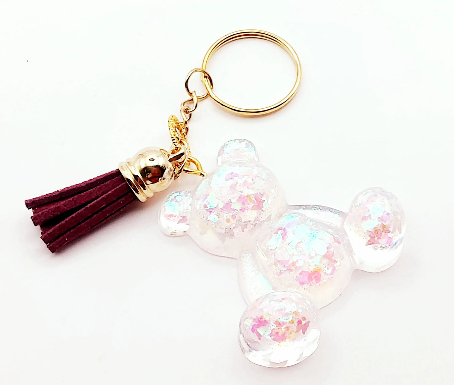 Porte-clés "Ourson assis" en résine époxy. Transparent et paillettes holographiques Papillons. Anneau doré. Pompon gland prune.