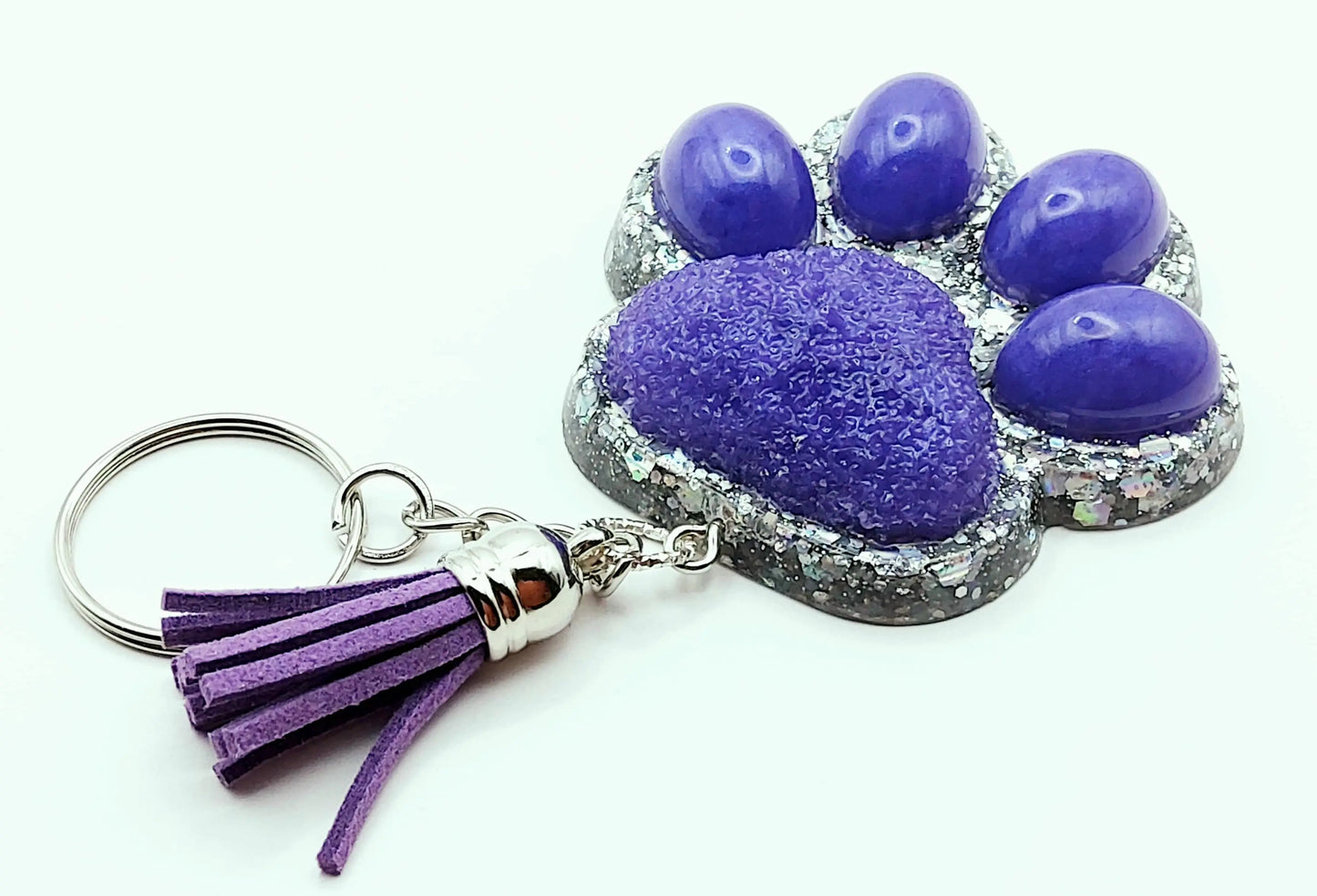 Porte-clés "Patte d'ours" en résine époxy. Violet et paillettes holographiques argentées. Anneau argenté, pompon gland violet.