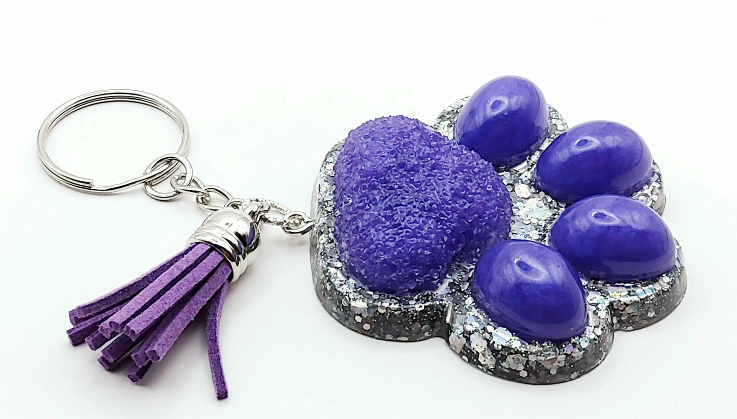 Porte-clés "Patte d'ours" en résine époxy. Violet et paillettes holographiques argentées. Anneau argenté, pompon gland violet.