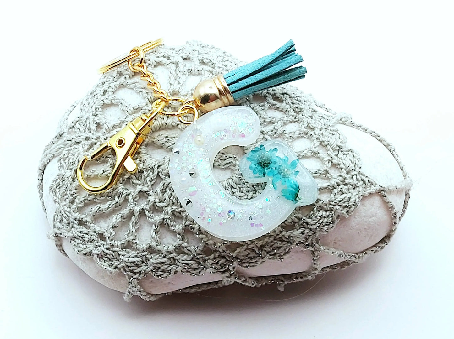 Porte-clés "Petite Lettre G" en résine, fleurs turquoise, posé sur un galet