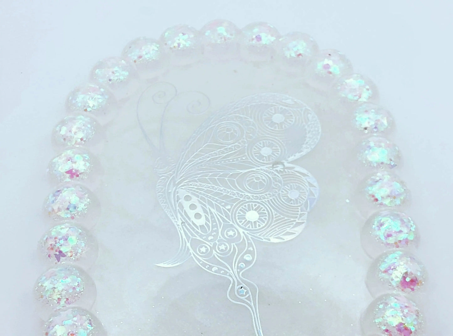 Vide-poches "Bulles" Ovale en résine époxy. Blanc, paillettes holographiques papillons en bordure. Grand papillon holographique au centre. Gros plan.