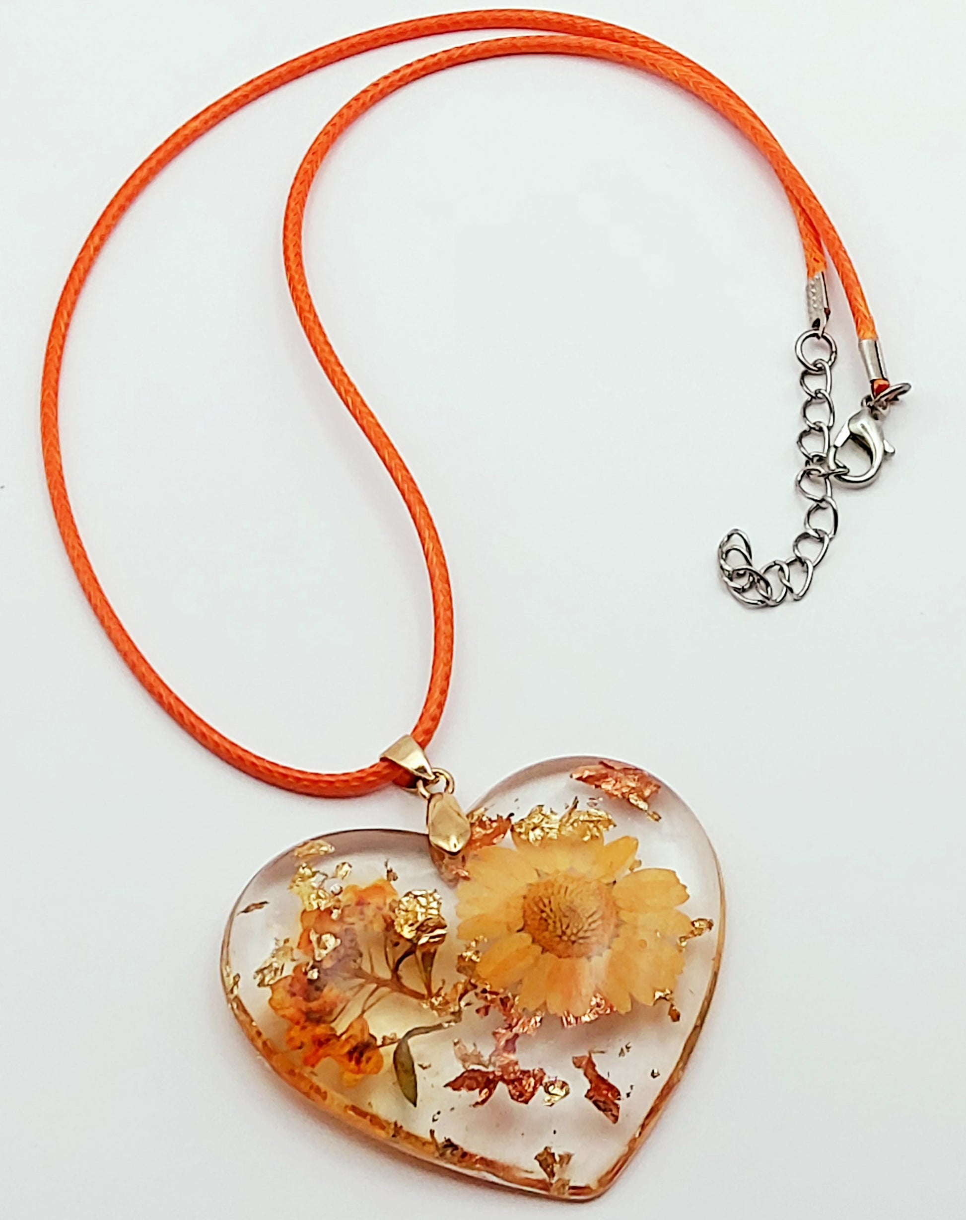 Pendentif "Coeur fleuri" en résine époxy, fleurs oranges. Cordon en coton ciré orange. Plan large.