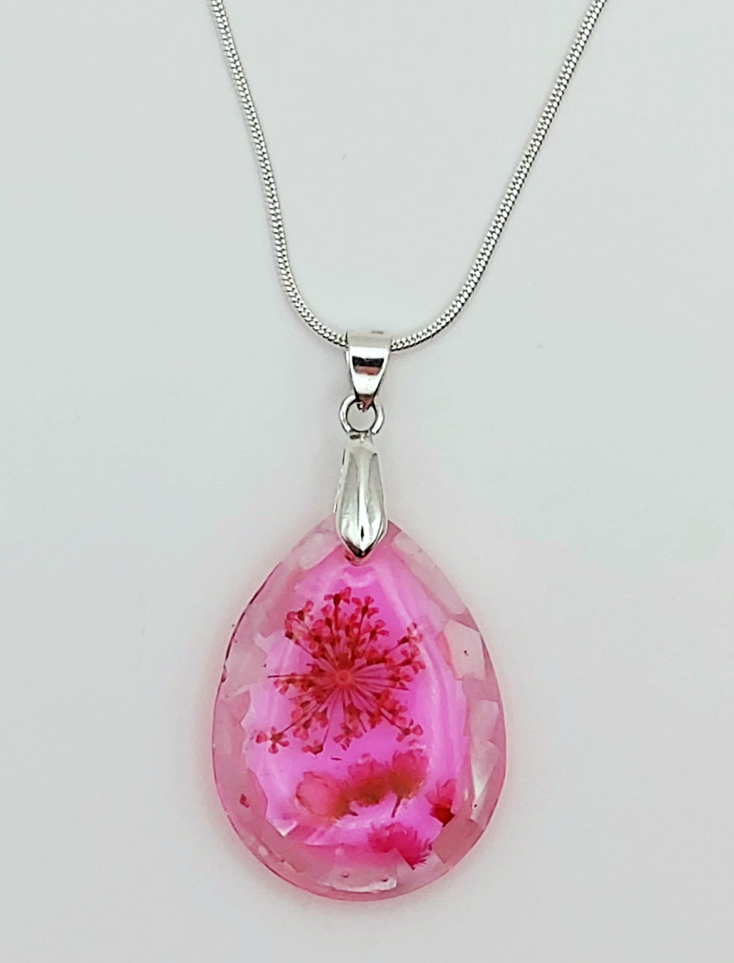 Pendentif "Goutte d'eau" en résine époxy et sa chaîne argentée. Fleurs et morceaux de coquillages roses. Gros plan.