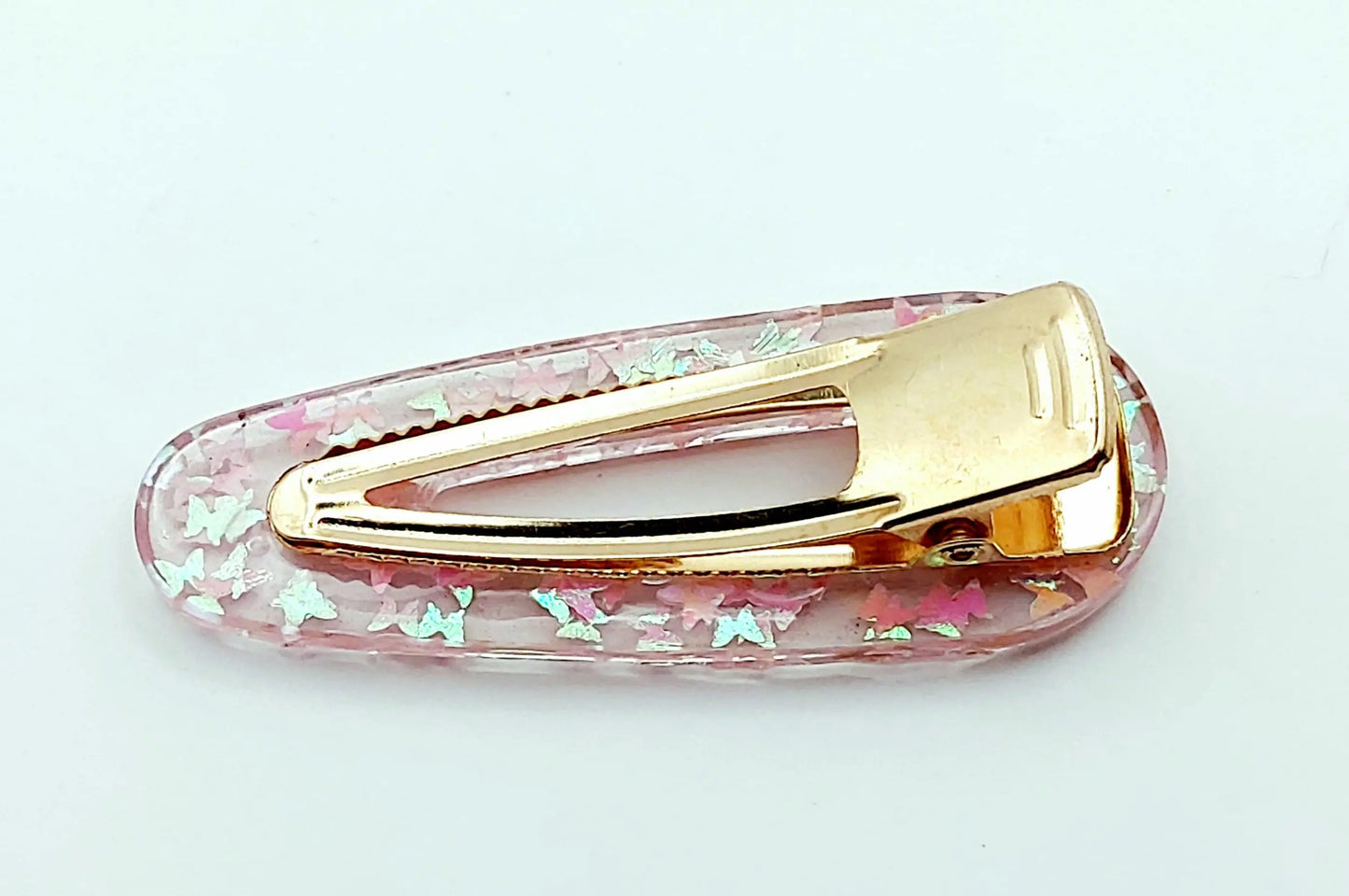 Barrette à cheveux "Arrondie" en résine époxy, paillettes papillons rose pâle. Vue de l'envers.