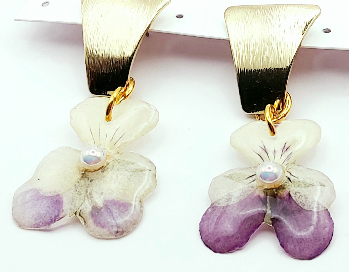 Boucles d'oreilles Fleurs de pensées en résine. Violet et blanc avec une perle blanche au centre. Apprêt doré.