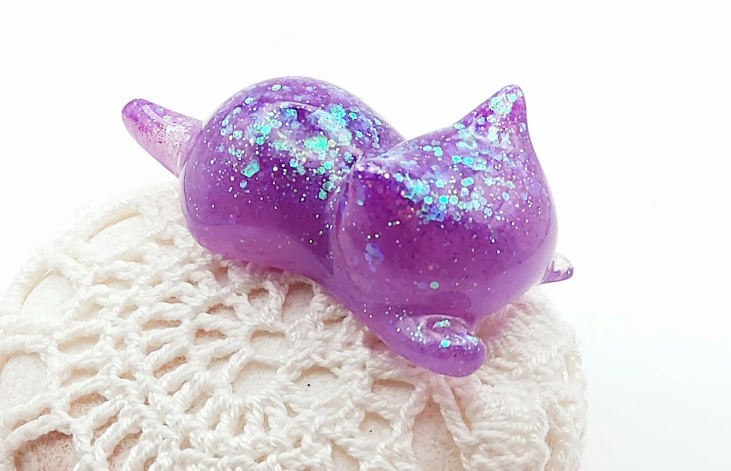 Figurine "Chaton couché" en résine époxy, mauve et paillettes holographiques. Posé sur un galet.