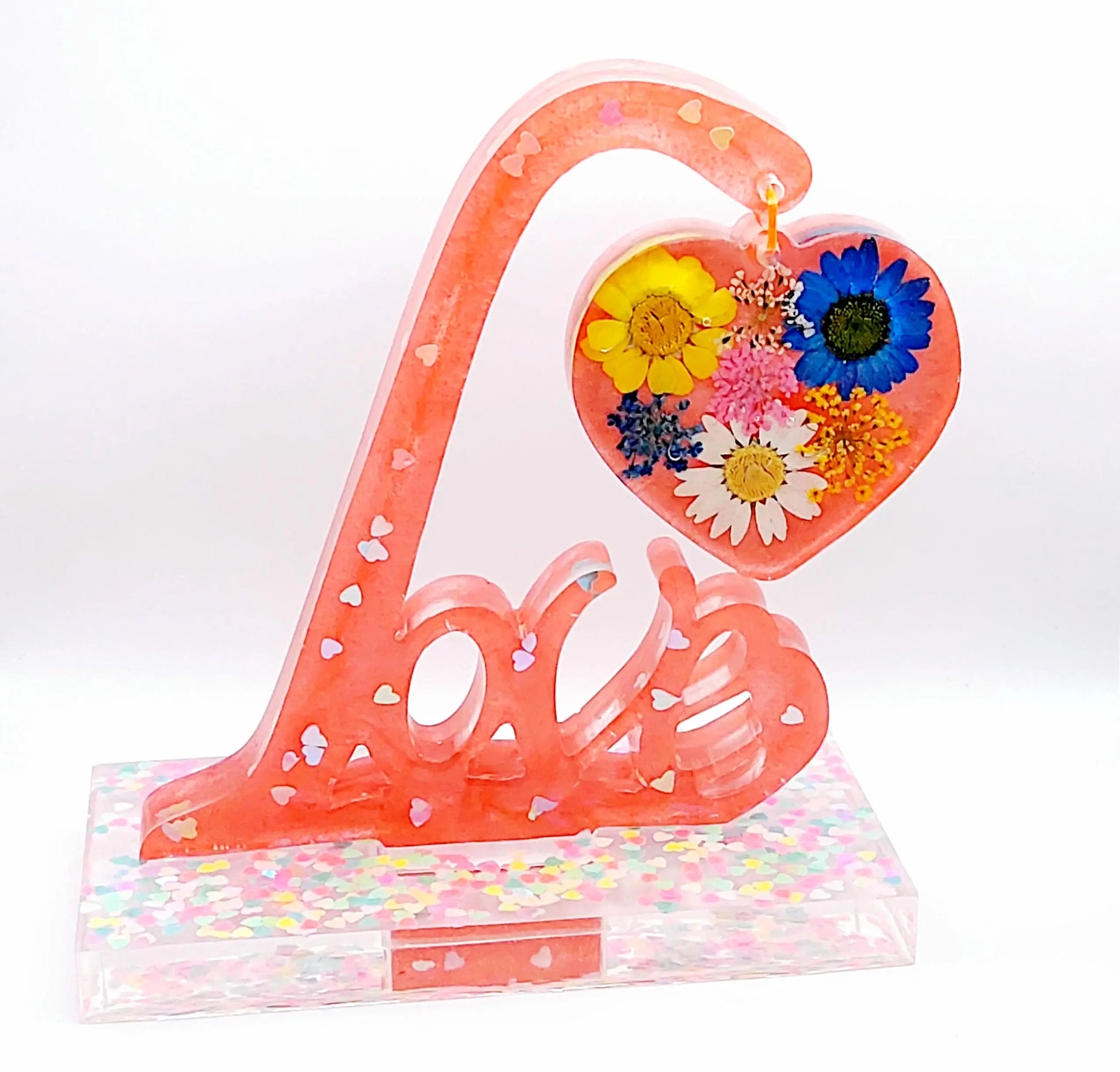 Mot décoratif LOVE sur socle en résine époxy. Rose avec paillettes coeurs holographiques et fleurs multicolores dans le coeur suspendu. Vue de face.