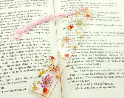 Marque-pages en résine et petites fleurs séchées roses, posé dans un livre