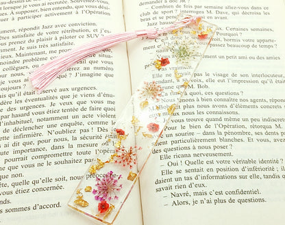 Marque-pages en résine et petites fleurs séchées roses, posé dans un livre