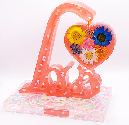 Mot décoratif LOVE sur socle en résine époxy. Rose avec paillettes coeurs holographiques et fleurs multicolores dans le coeur suspendu.