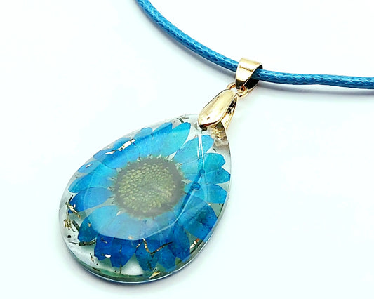 Pendentif OVALE en résine époxy. Fleur bleue et paillettes dorées. Cordon en coton ciré bleu.