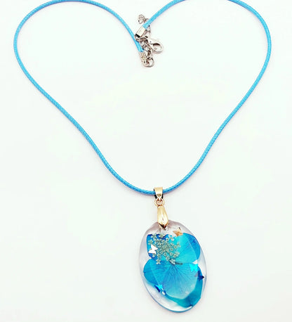 Pendentif OVALE en résine époxy. Fleurs bleue et blanche. Cordon en coton ciré bleu. PRETTY RESINE