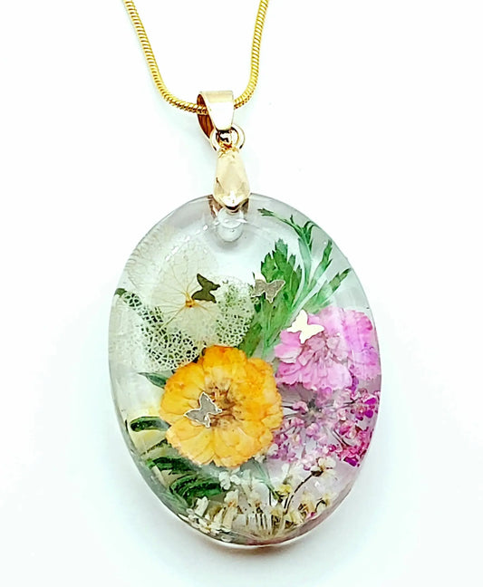 Pendentif Ovale en résine époxy et sa chaîne dorée. Fleurs multicolores et papillons dorés. Gros plan.