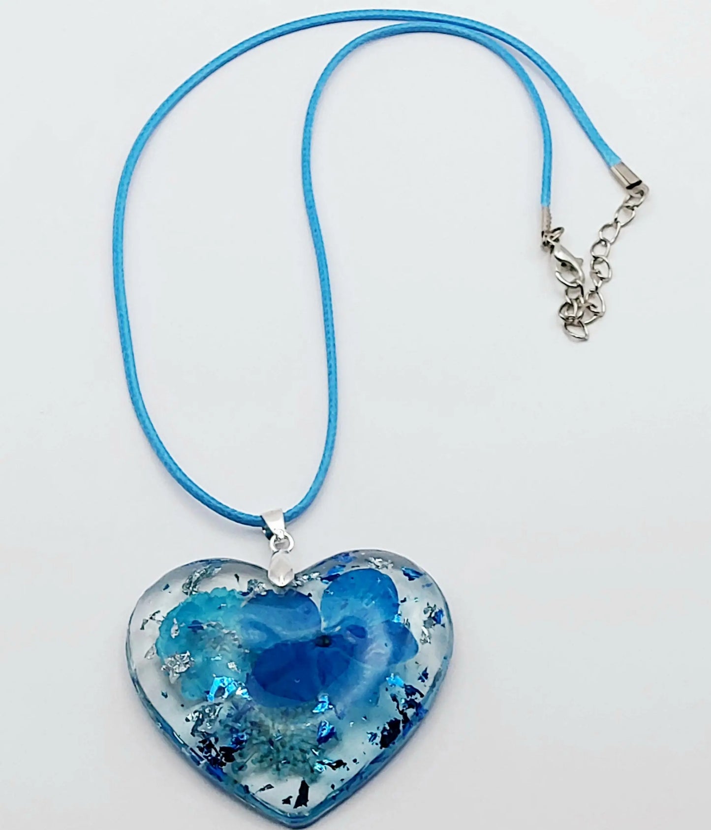 Pendentif "Coeur Fleuri" en résine époxy, fleurs et cordon en coton ciré bleus, plan large.