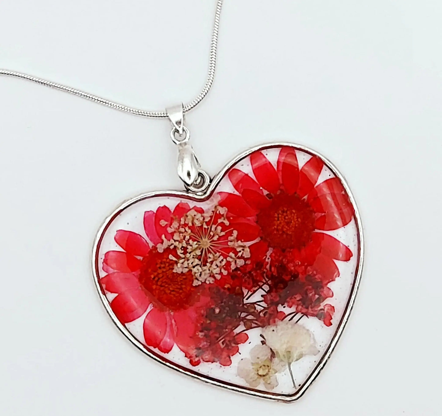 Pendentif Coeur argenté en résine et sa chaîne. Fleurs rouges et blanches. Gros plan.