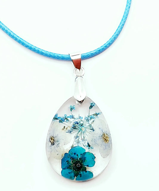 Pendentif "Goutte d'eau" en résine époxy,. Transparent avec fleurs bleues. Cordon en coton ciré bleu clair. Gros plan.