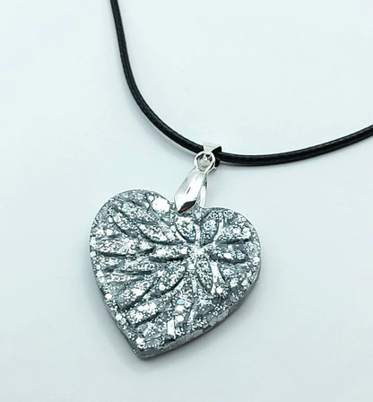 Pendentif "Petit Coeur" en résine époxy, paillettes argentées, cordon en coton ciré noir. Gros plan.