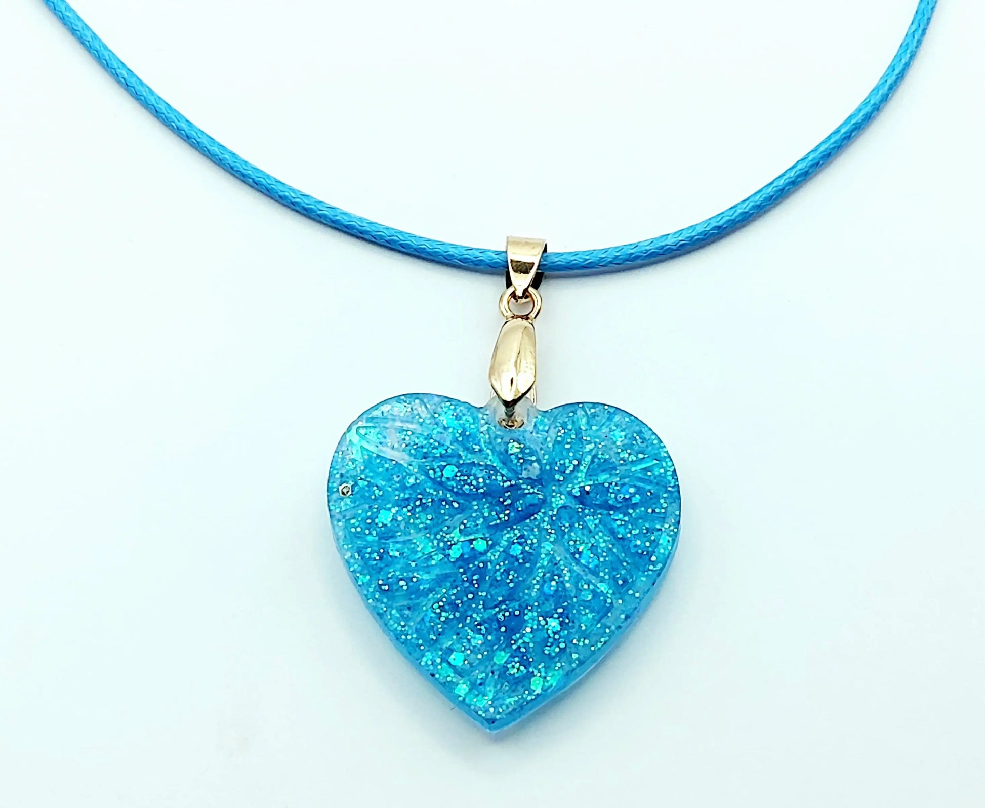 Pendentif "Petit Coeur" en résine époxy, paillettes bleues. Cordon en coton ciré bleu. Gros plan.