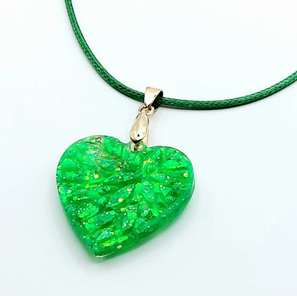 Pendentif "Petit Coeur" en résine époxy, paillettes vertes. Cordon en coton ciré vert. Gros plan.