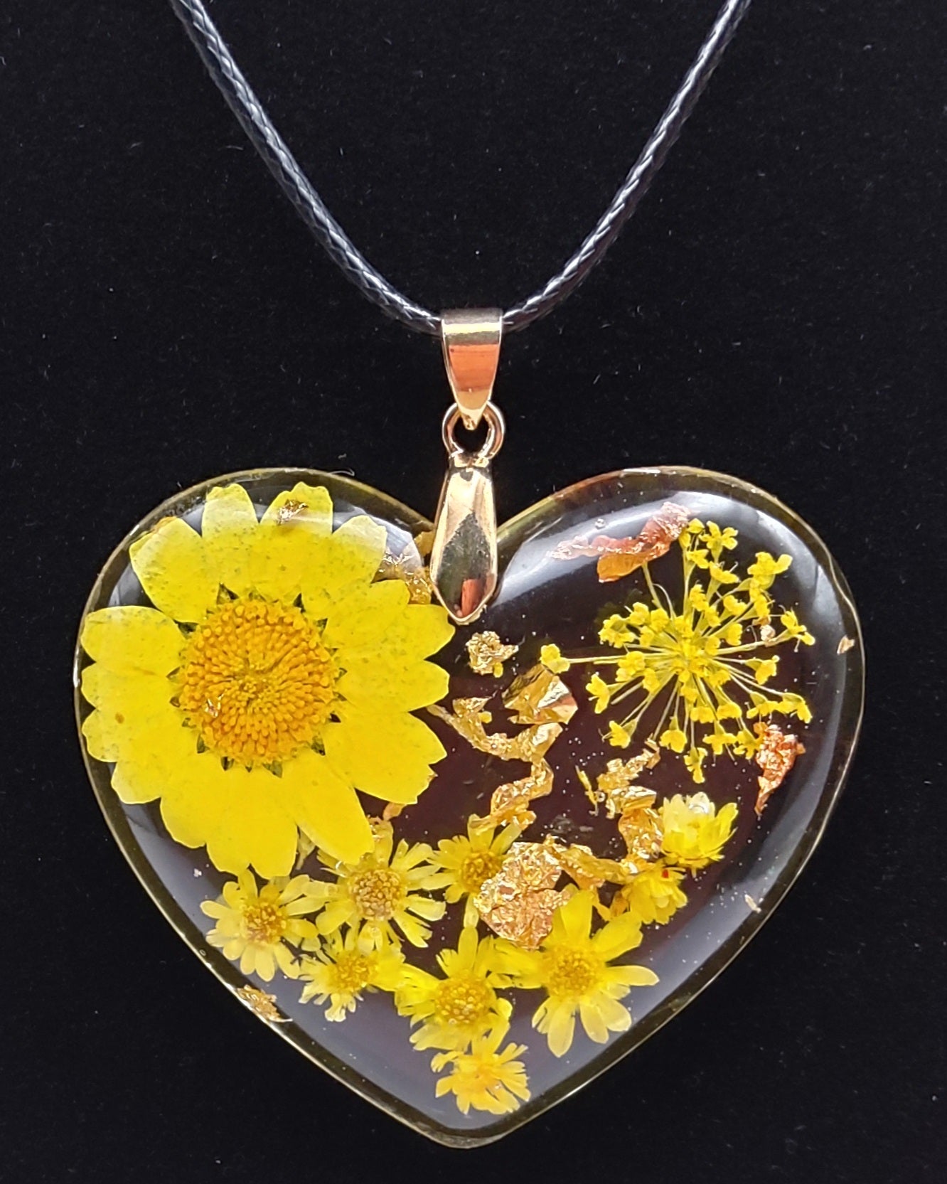 Pendentif "Coeur Fleuri" en résine époxy, fleurs jaunes. Gros plan sur fond noir. Cordon en coton ciré noir.