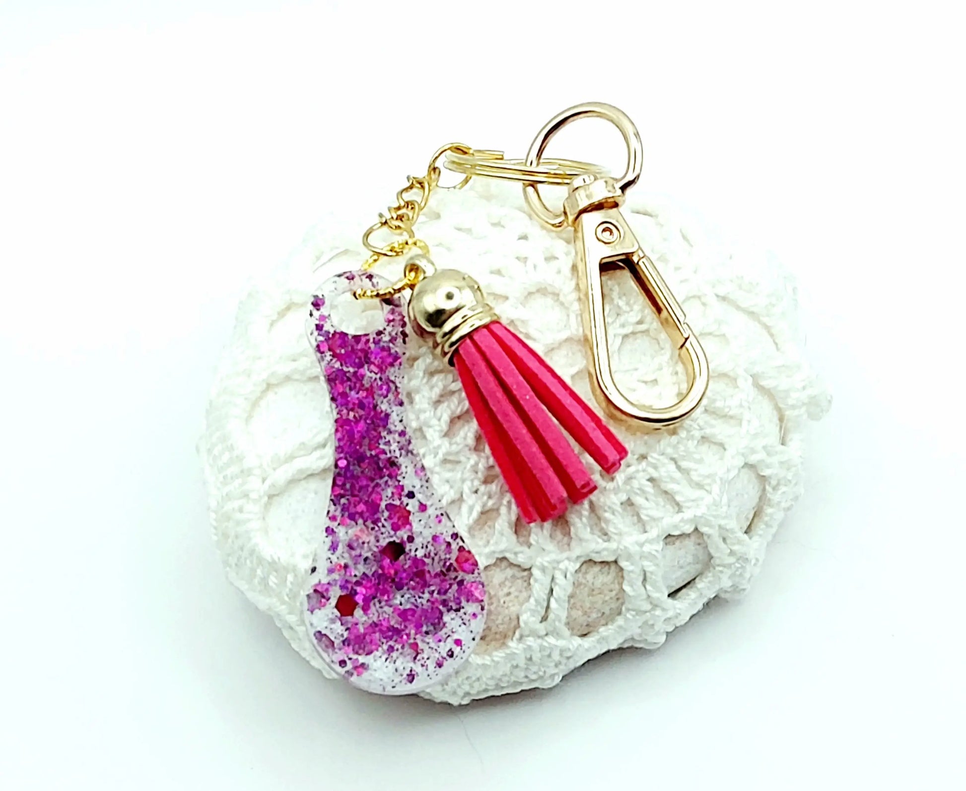 Porte-clés Jeton de caddie en résine époxy, blanc irisé et paillettes fuchsia. Pompon gland rose fuchsia, Anneau et mousqueton doré. Posé sur un galet.