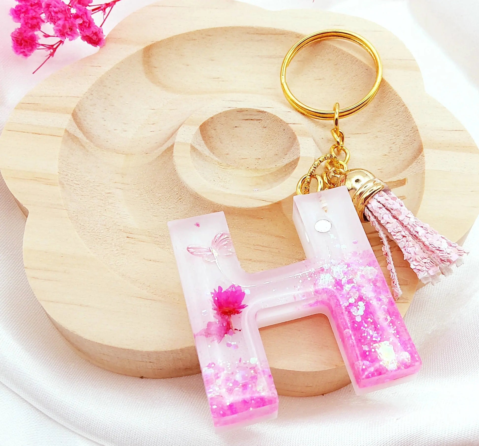 Porte-clés LETTRE H en résine époxy. Fond blanc. Paillettes, fleurs et papillon roses. Pompon gland pailleté rose - PRETTY RESINE